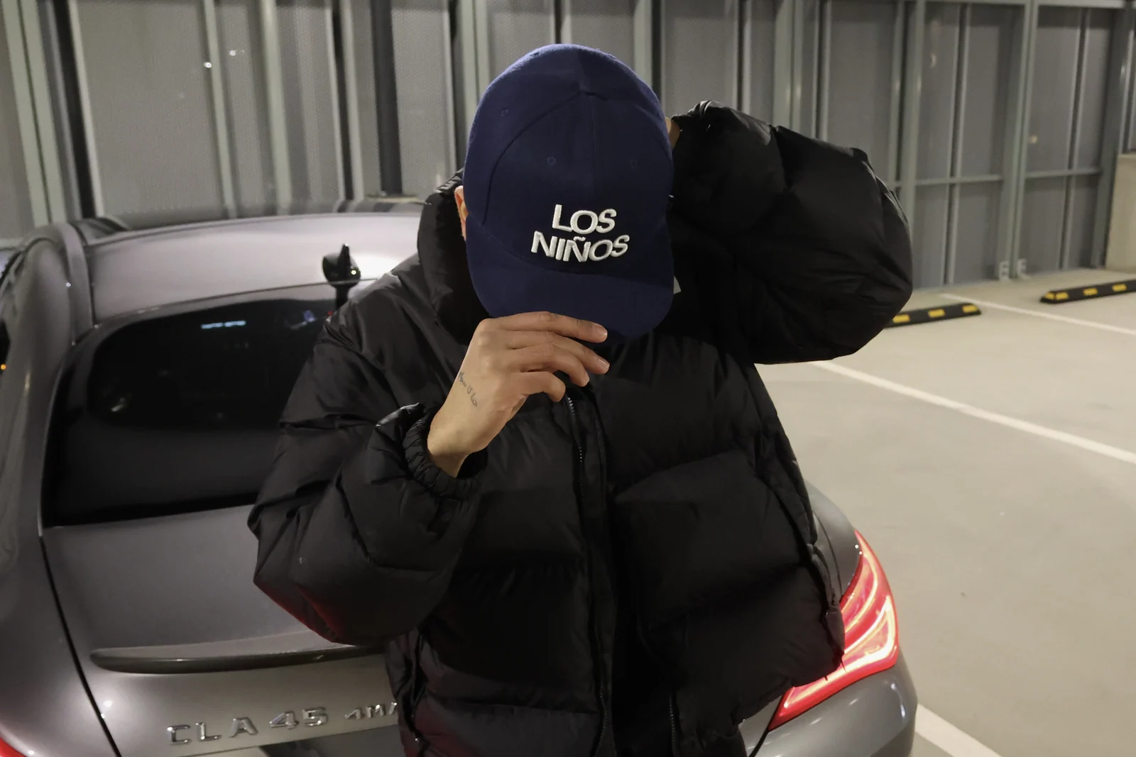 The navy Los Niños hat worn close to the camera beside a car.